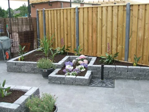 Verhoogde plantenbak van stapelblokken met bloeiende beplanting voor een houten schutting